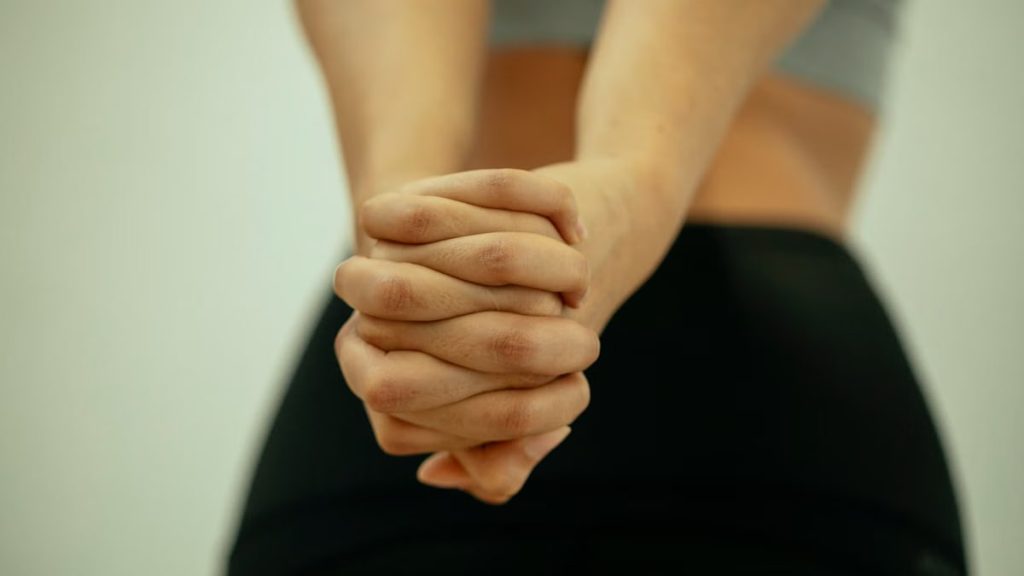 Back view of crop unrecognizable fit female in sportswear stretching arms and shoulders with fingers locked behind back before yoga session